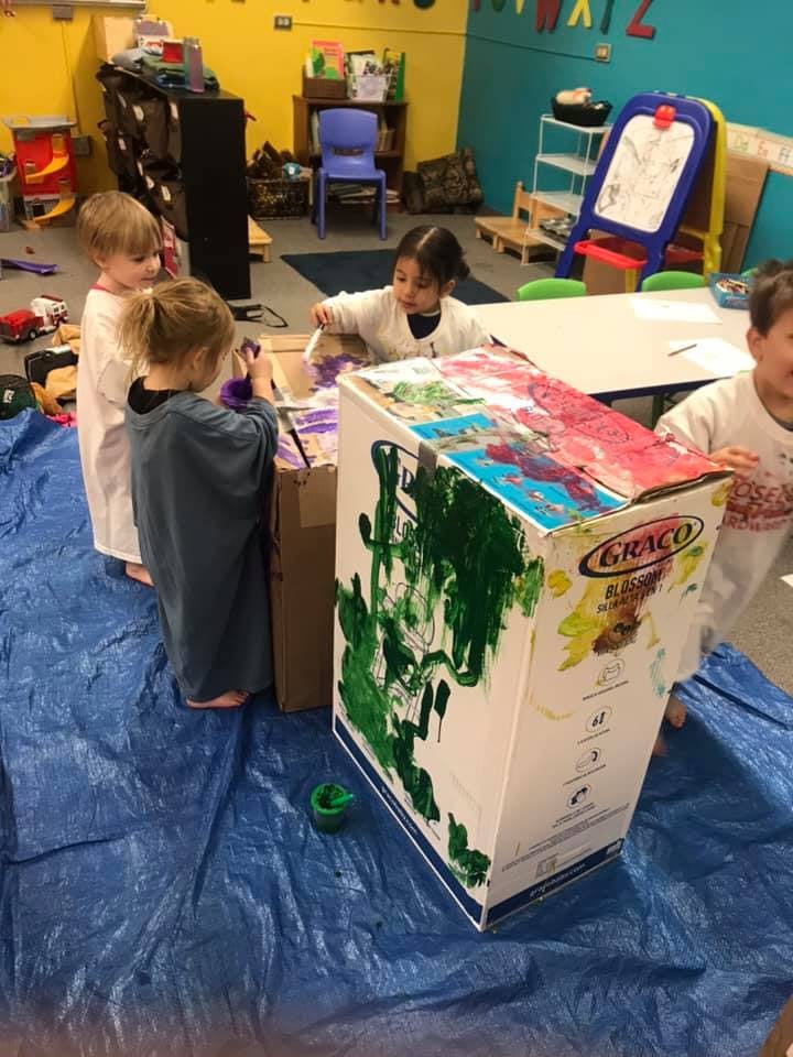 Children painting a large cardboard box in a classroom