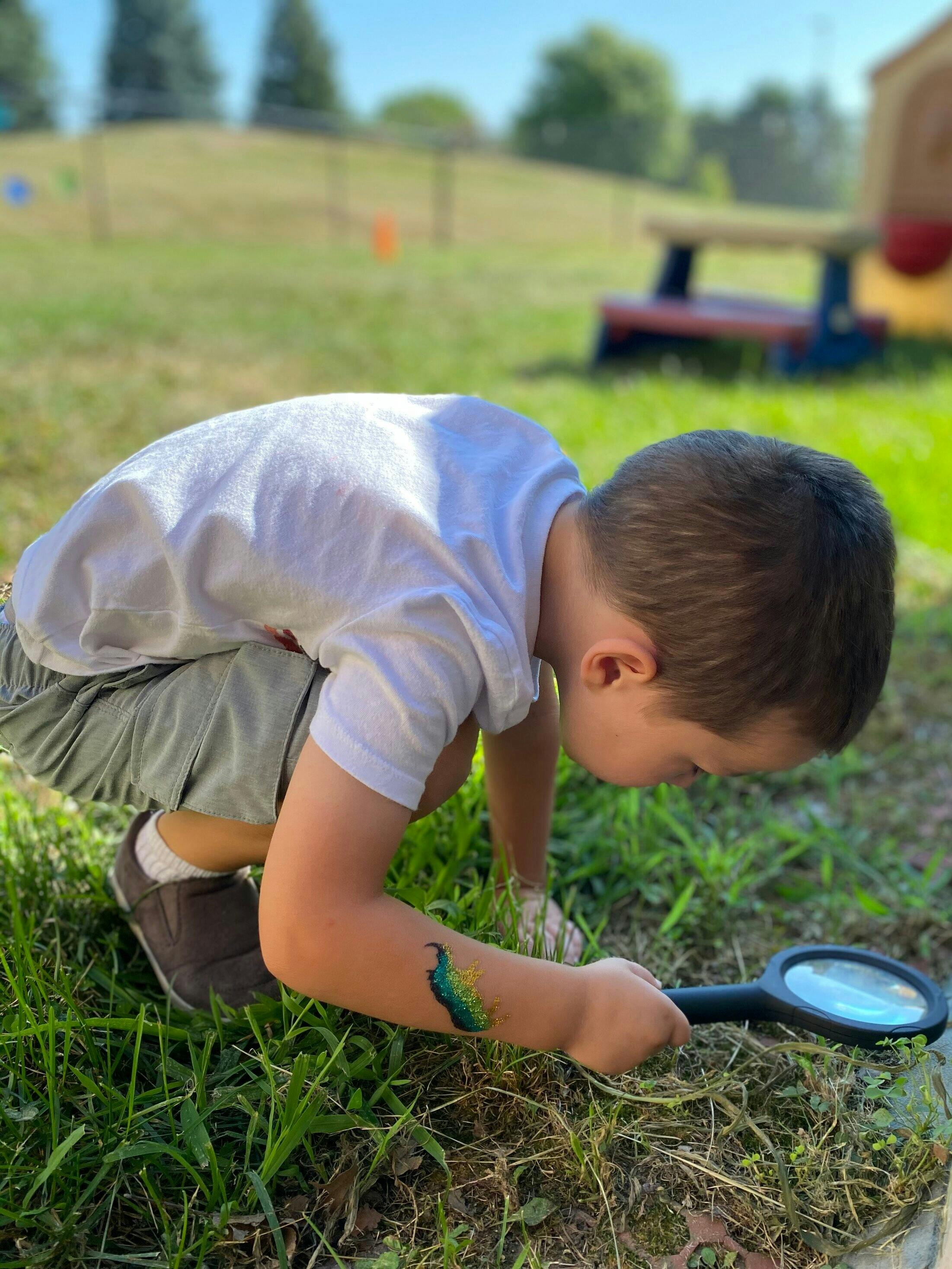 Child crouching in grass and using a magnifying glass