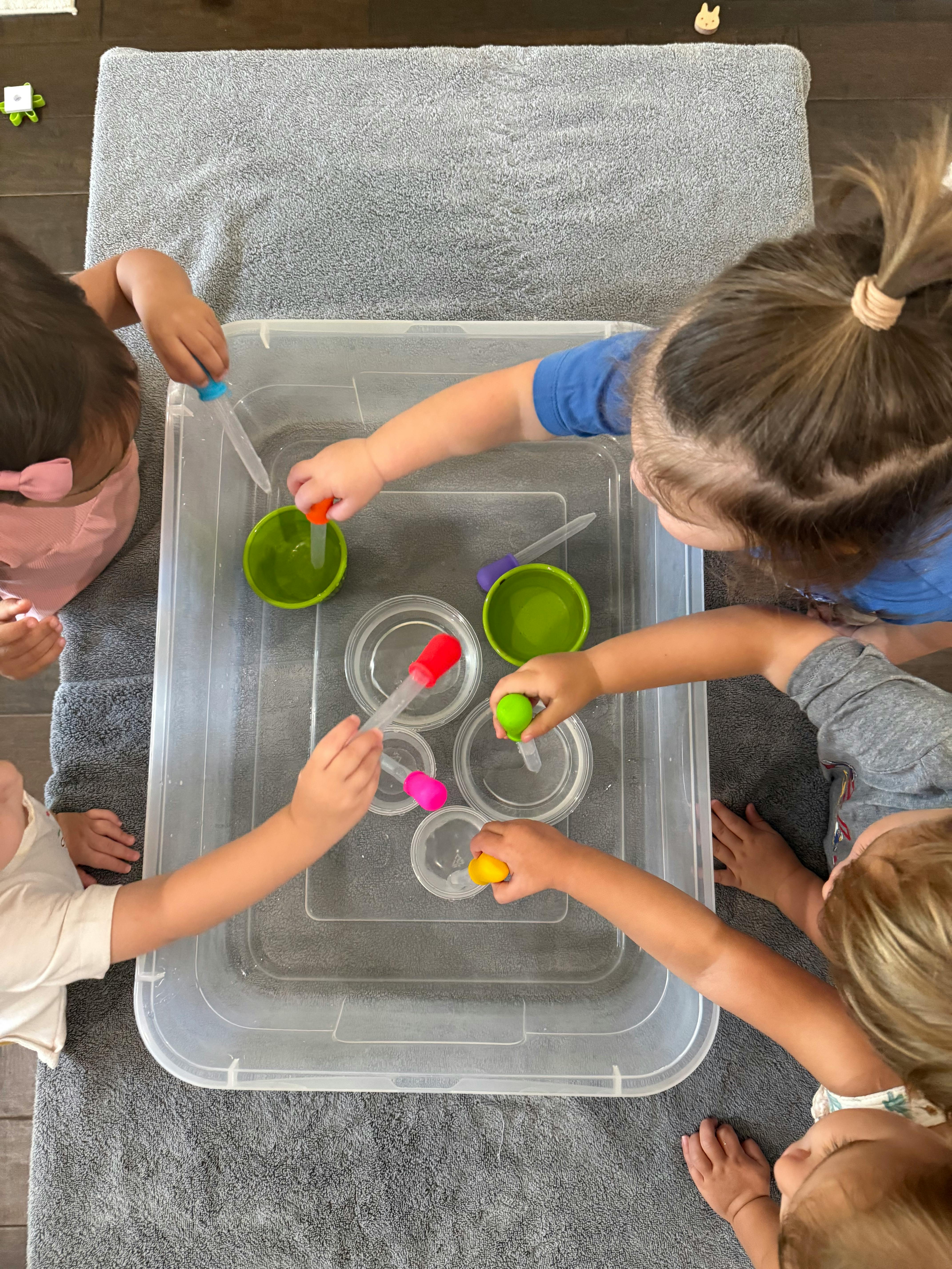 Children playing with pipettes and bowls in a clear bin