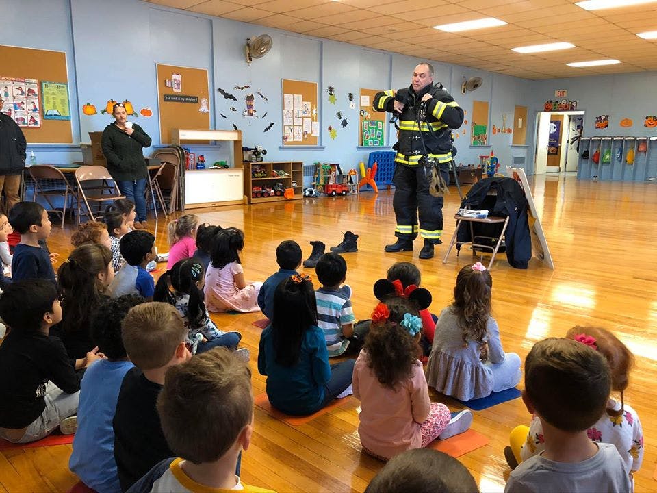 Firefighter speaking to a group of children sitting on the floor in a classroom