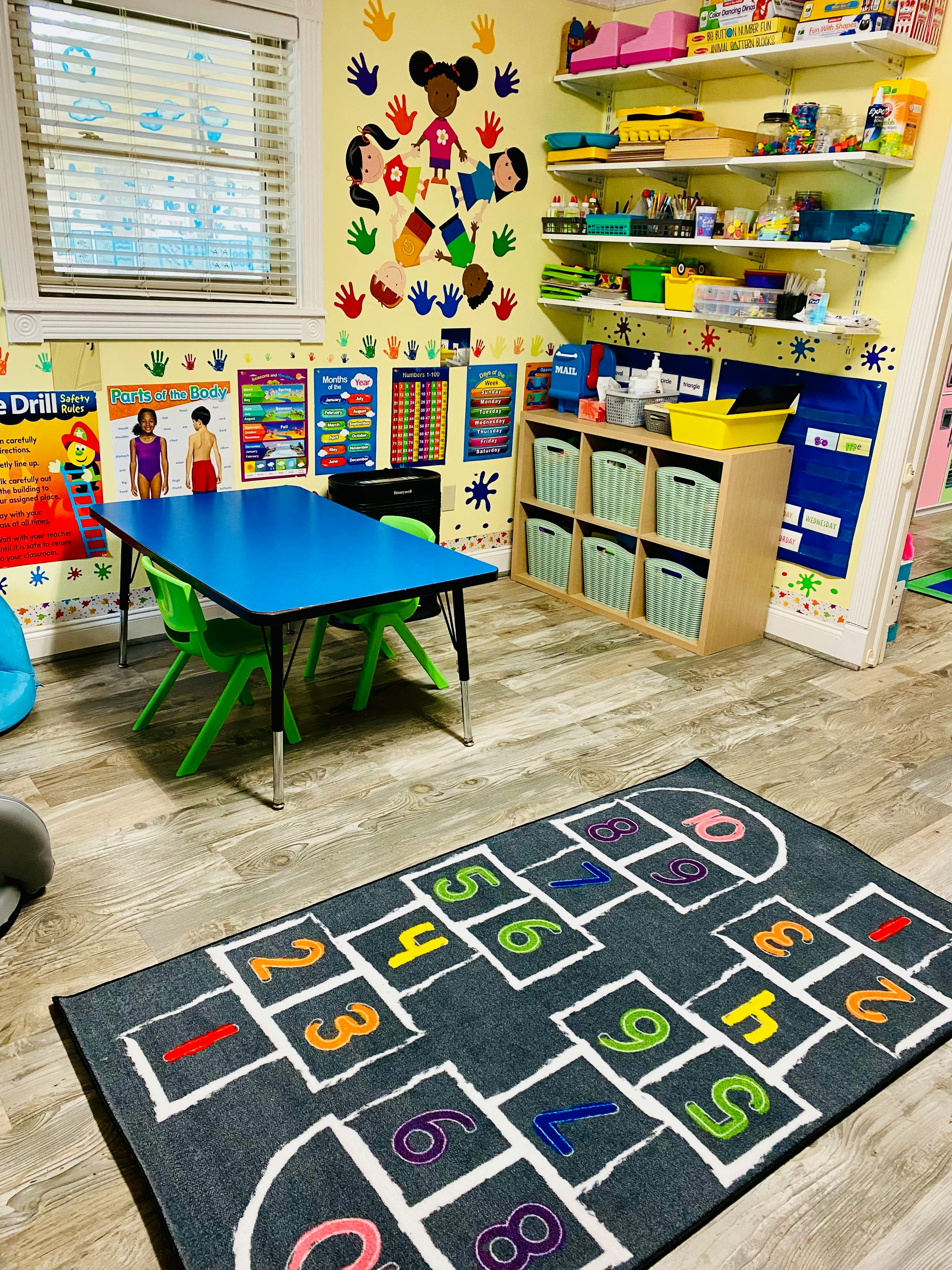 Classroom with a small blue table, green chairs, and a hopscotch rug