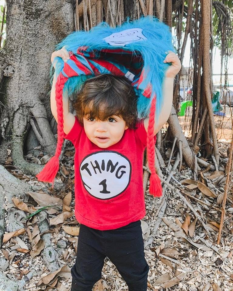 Child in red Thing 1 shirt holding a blue furry hat over their head