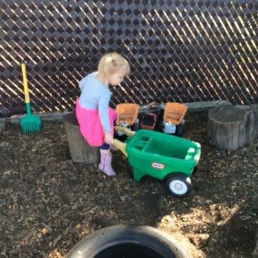 Child playing with a toy wheelbarrow and trucks outdoors