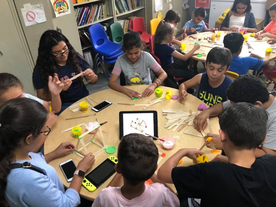 Adult and children at a table making crafts with sticks and small objects
