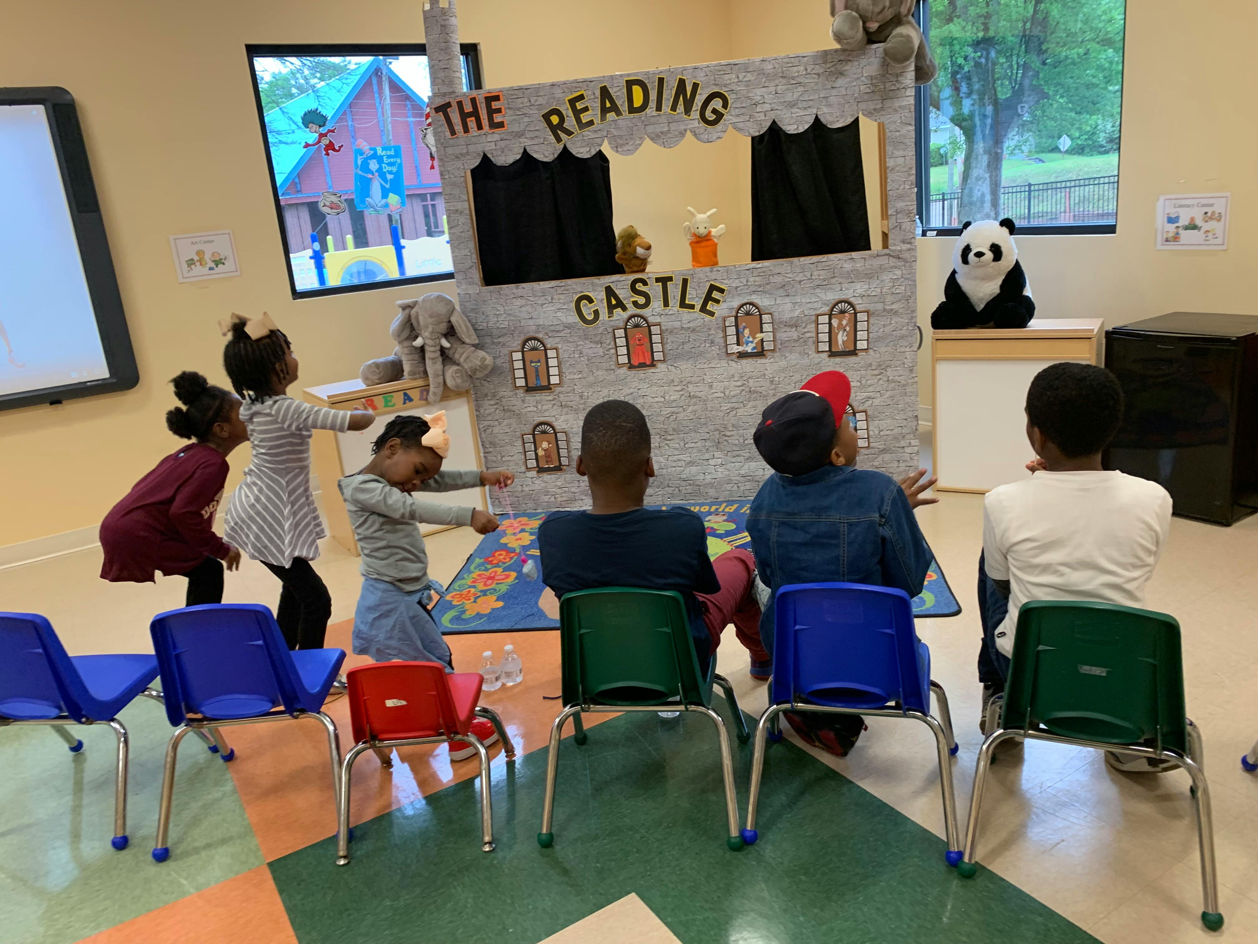 Children performing in front of a puppet stage that says "The Reading Castle"