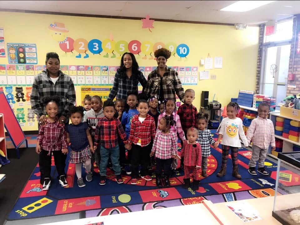 Three adults and many children standing together in a classroom