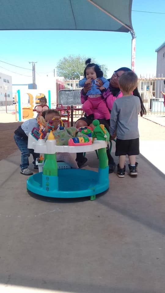 Adult holding a child, with other children playing around a baby activity center
