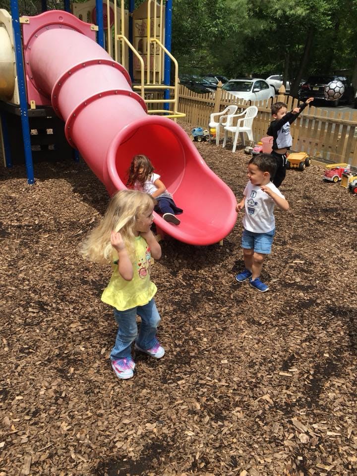 Children playing on a pink slide and wood chips at a playground