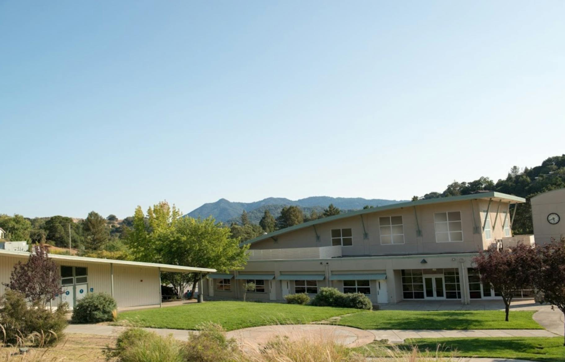 Two buildings with green lawns and trees, mountains in the background