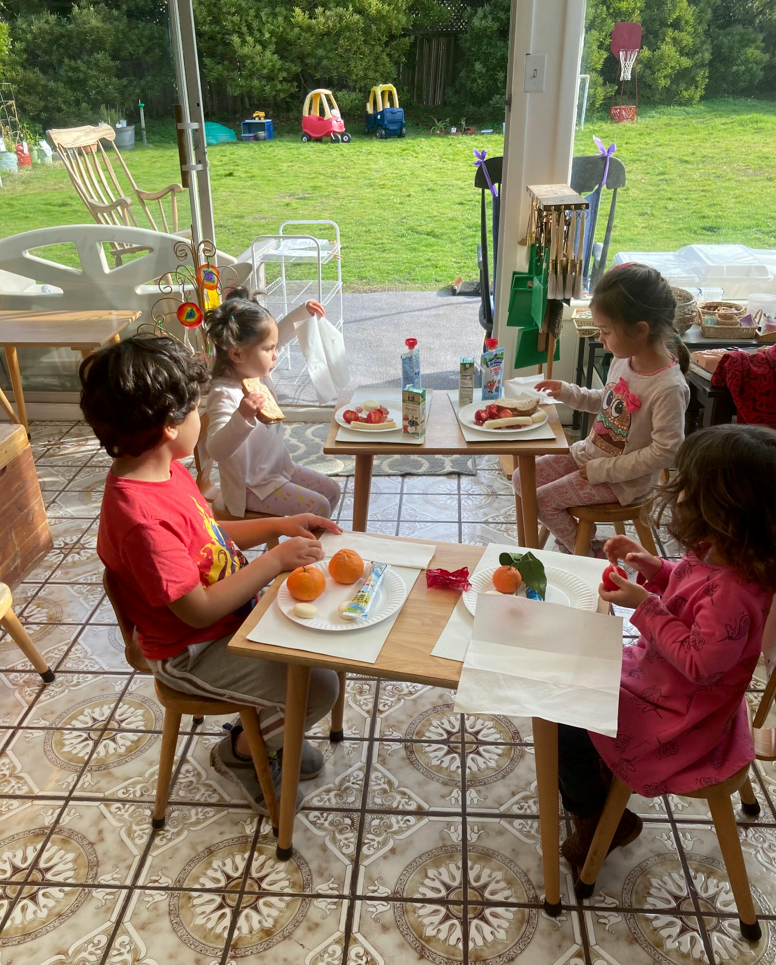 Four children sitting at small tables with food and drinks