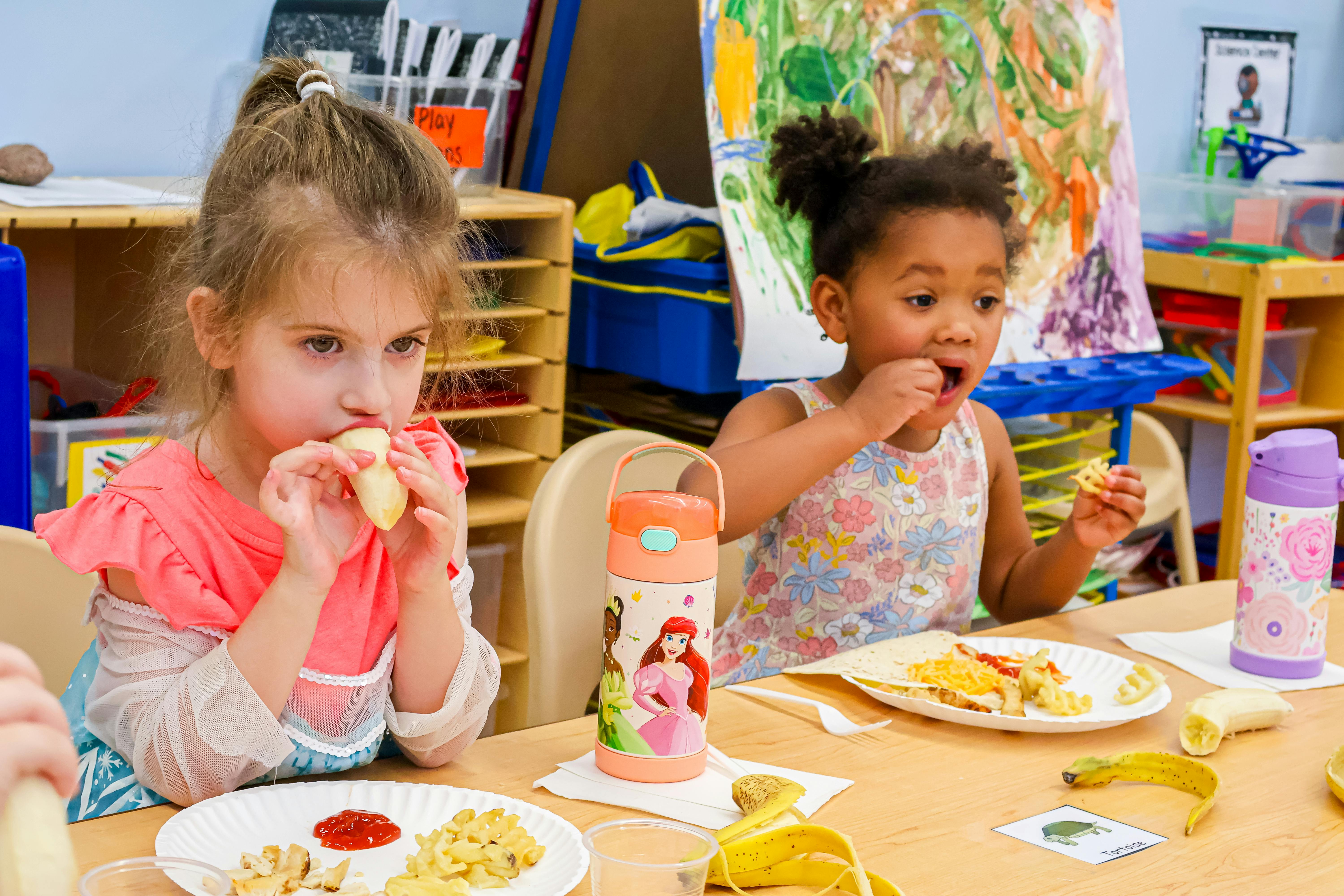 Two children eating at a table in a classroom