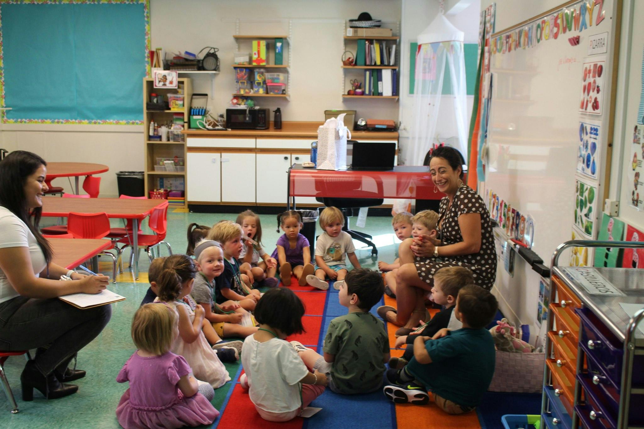Two adults with a group of children sitting on the floor in a classroom