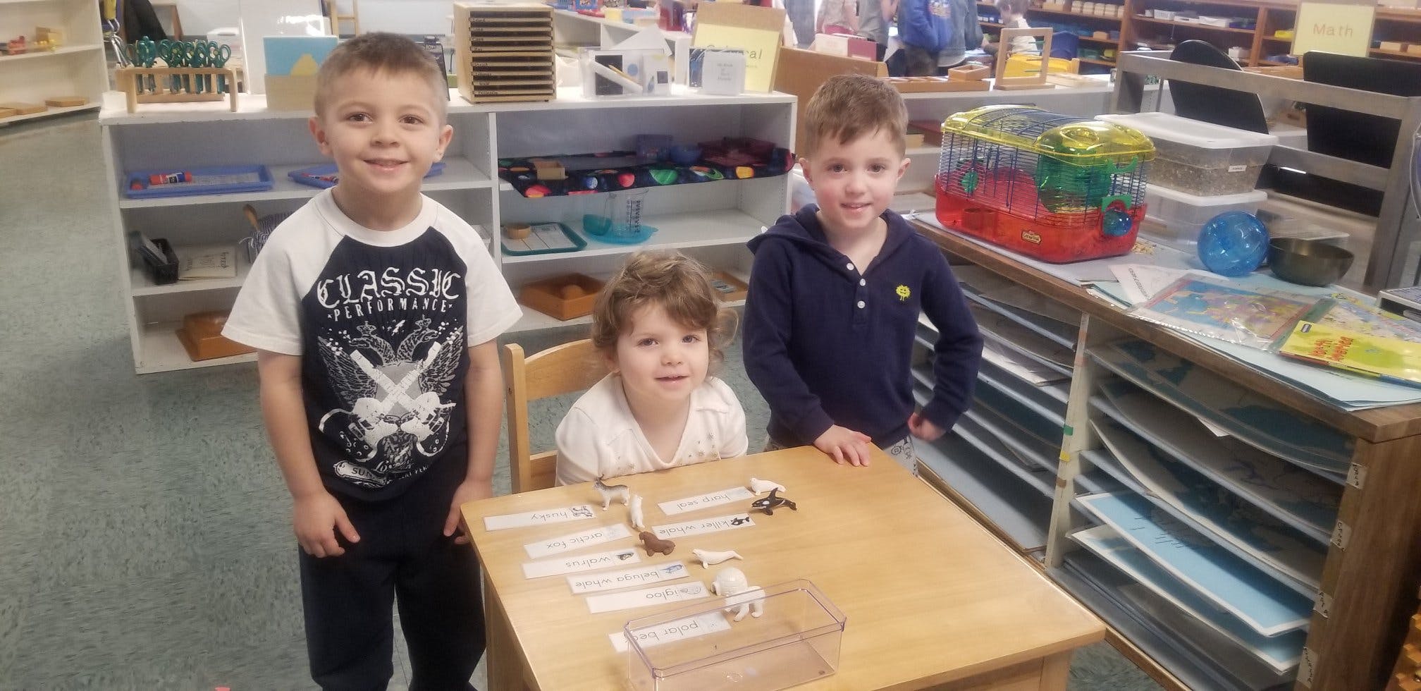Three children standing around a table in a classroom