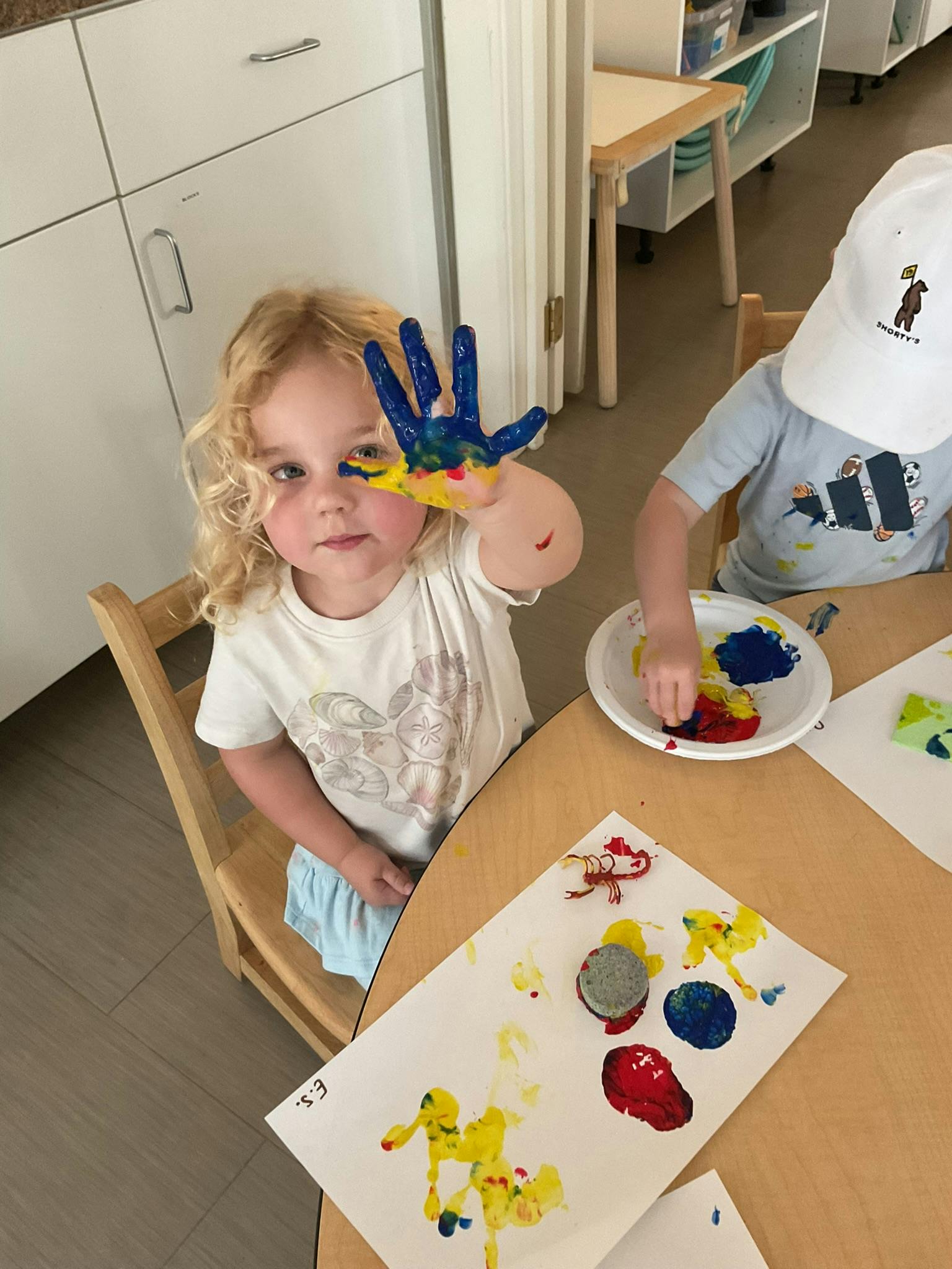 Child showing a hand covered in blue and yellow paint at a table