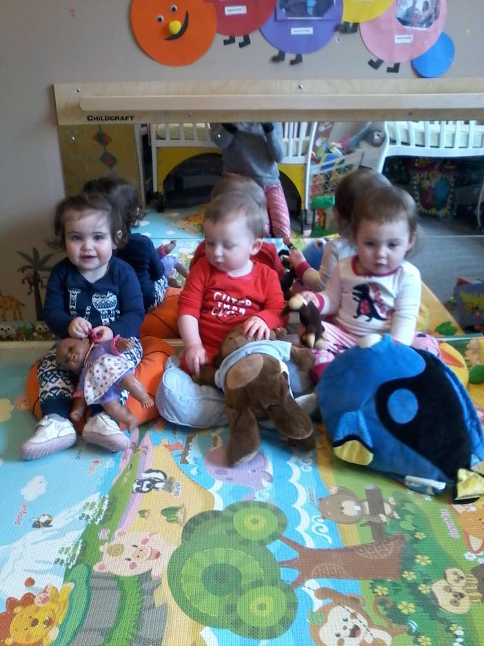 Three children sitting on a playmat with stuffed animals and dolls