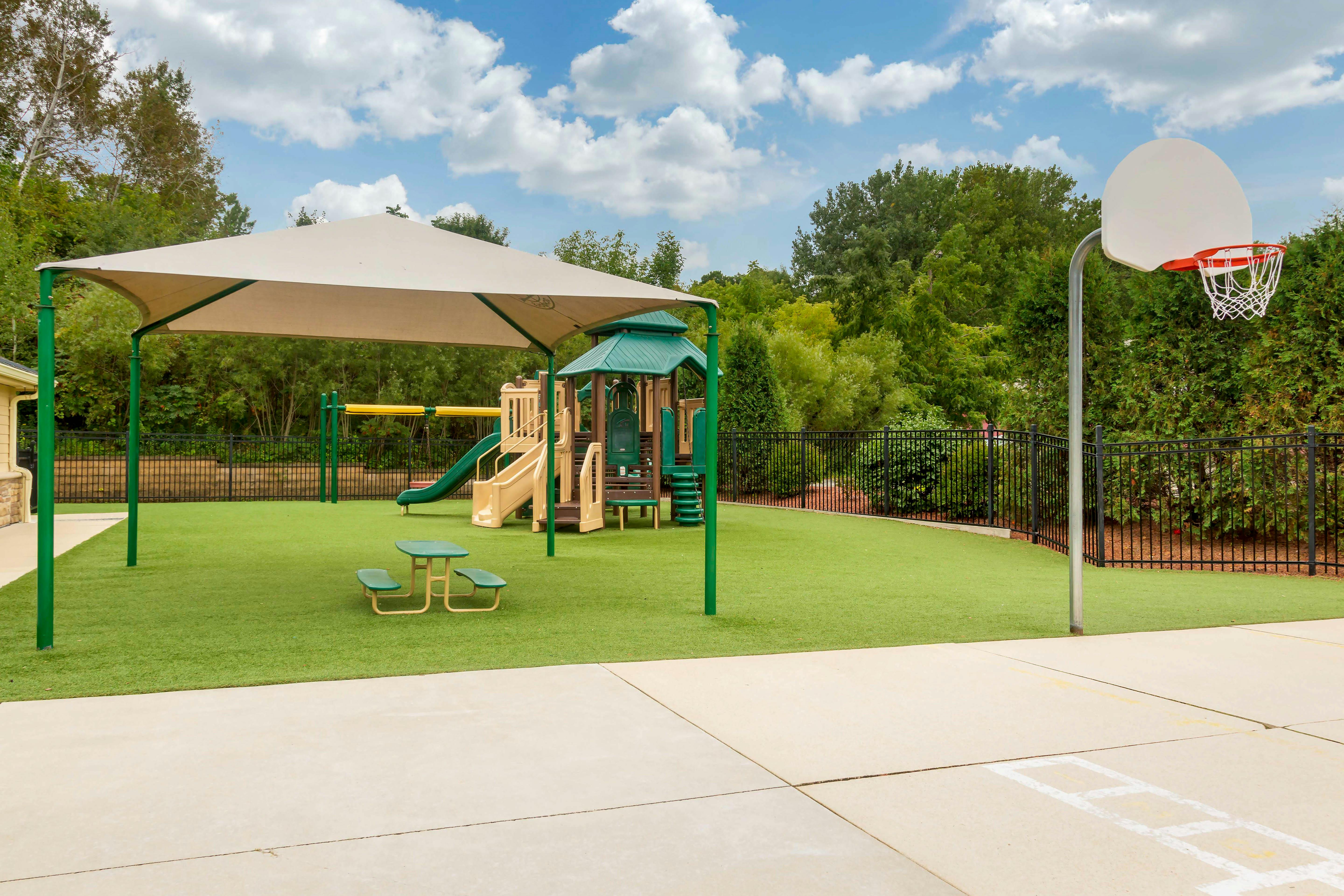 An outdoor playground with artificial turf, a play structure, and a basketball hoop