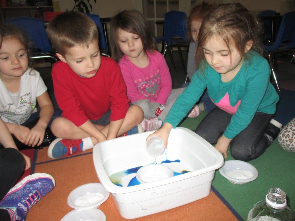 Children gathered around a tub, one child pouring water into it