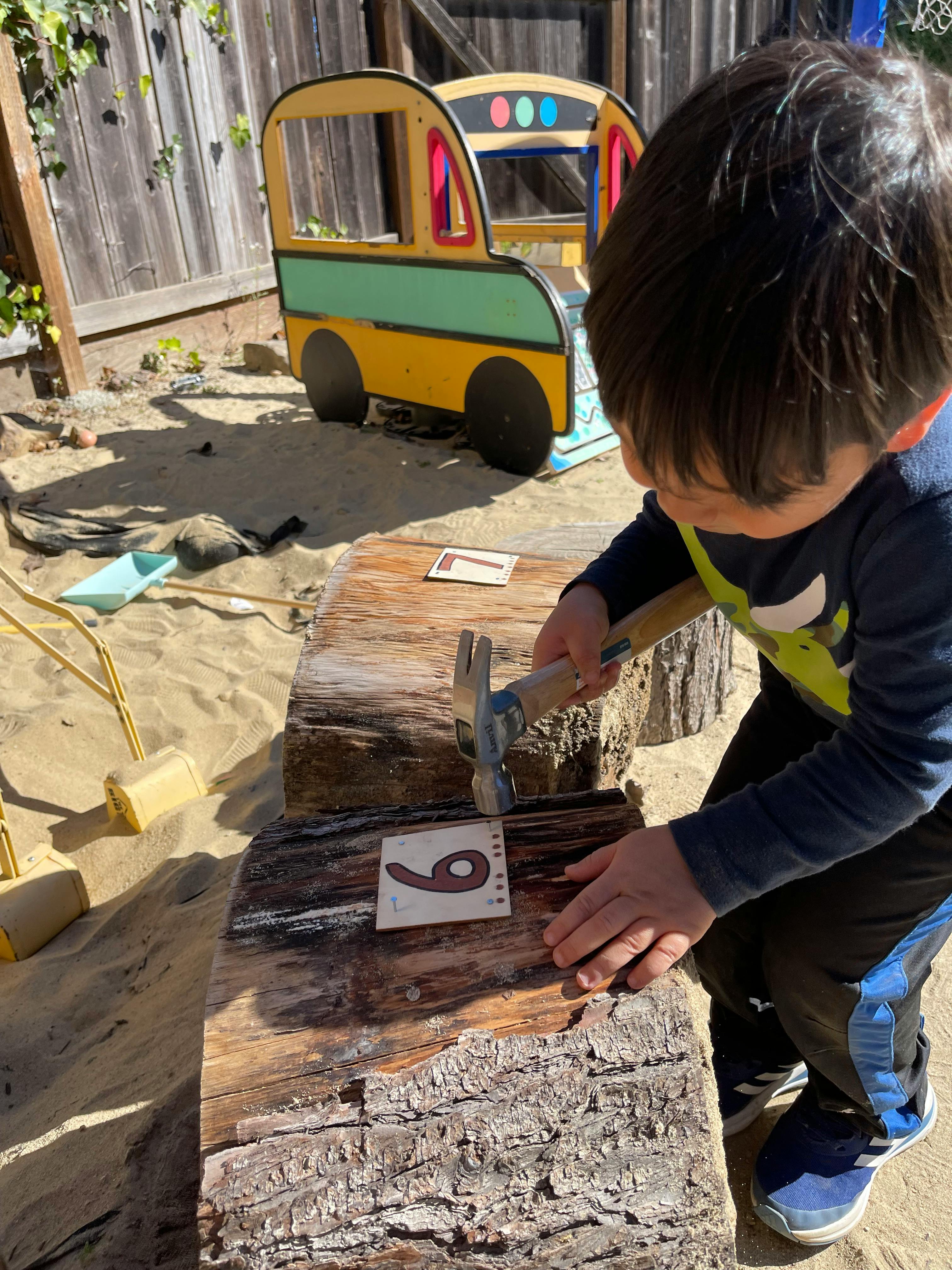 Child hammering a nail into a wooden log with a number 9 card
