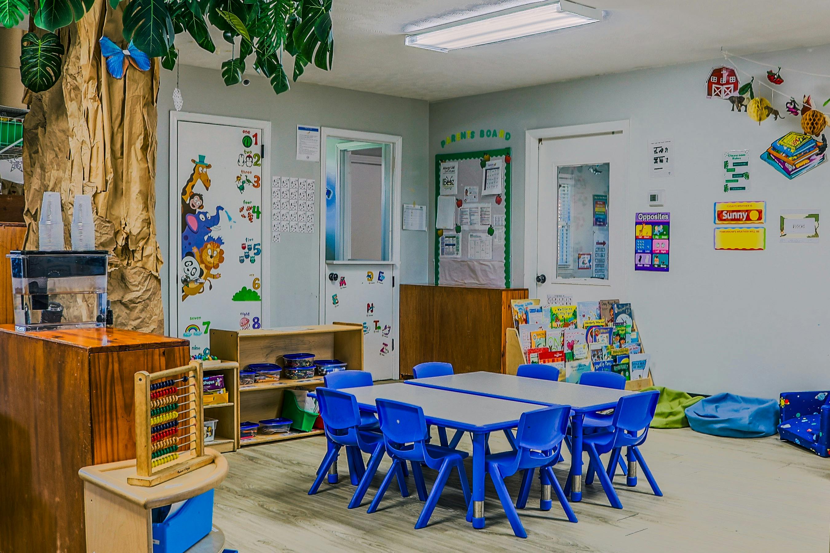 Empty preschool classroom with small tables and blue chairs