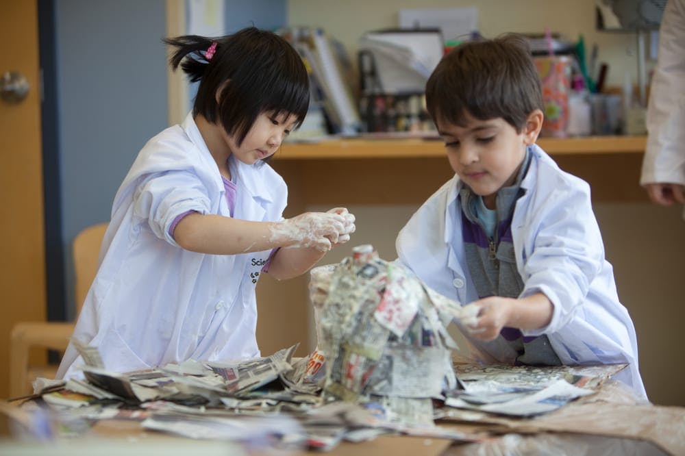 Two children in lab coats doing paper mache