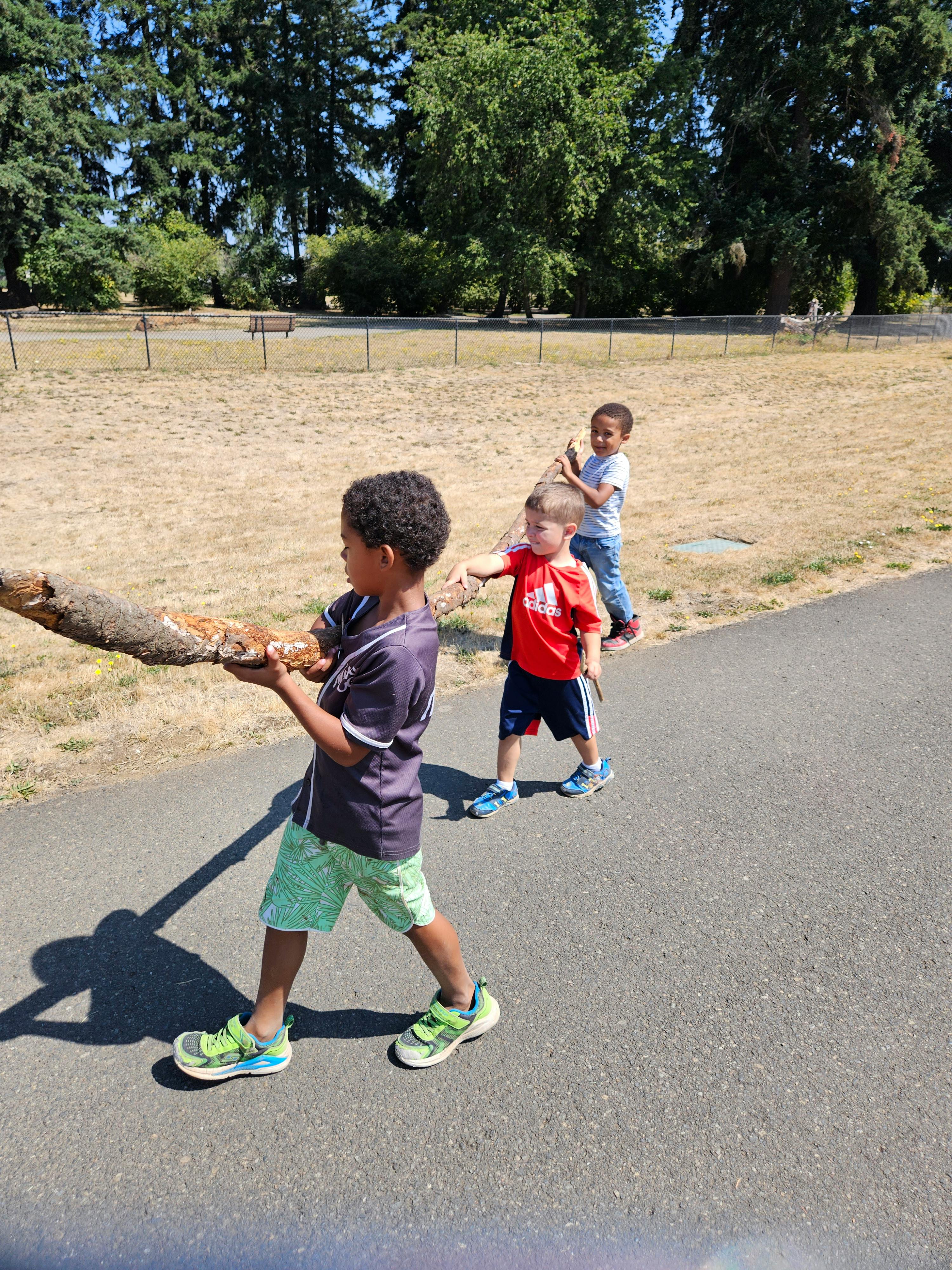Three children holding a long stick while walking on a path
