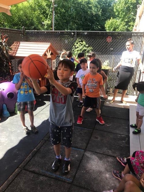 Child holding a basketball with other children and an adult nearby