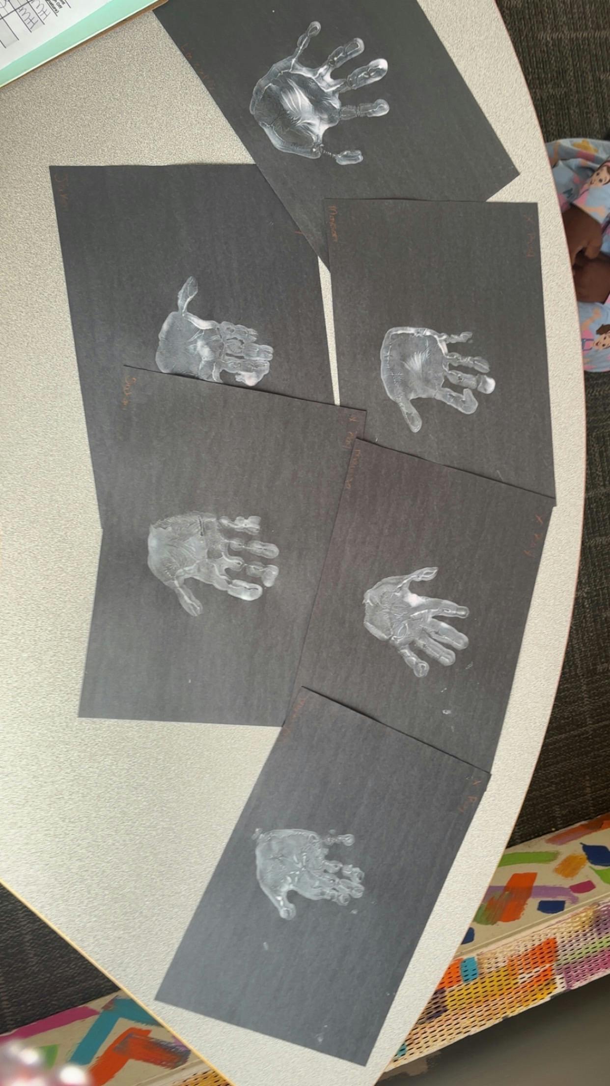 White handprints on black paper arranged on a table