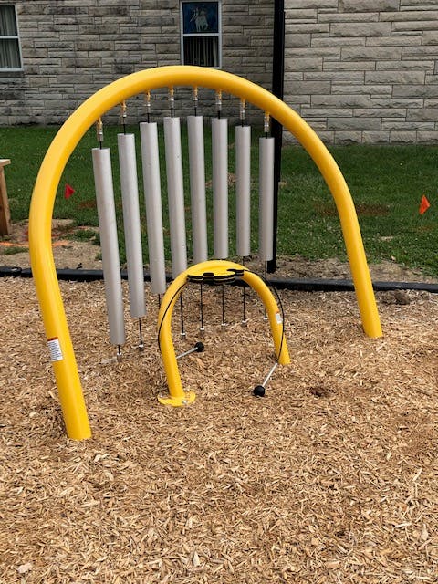 Outdoor musical instruments with yellow frames and metal chimes on wood chips