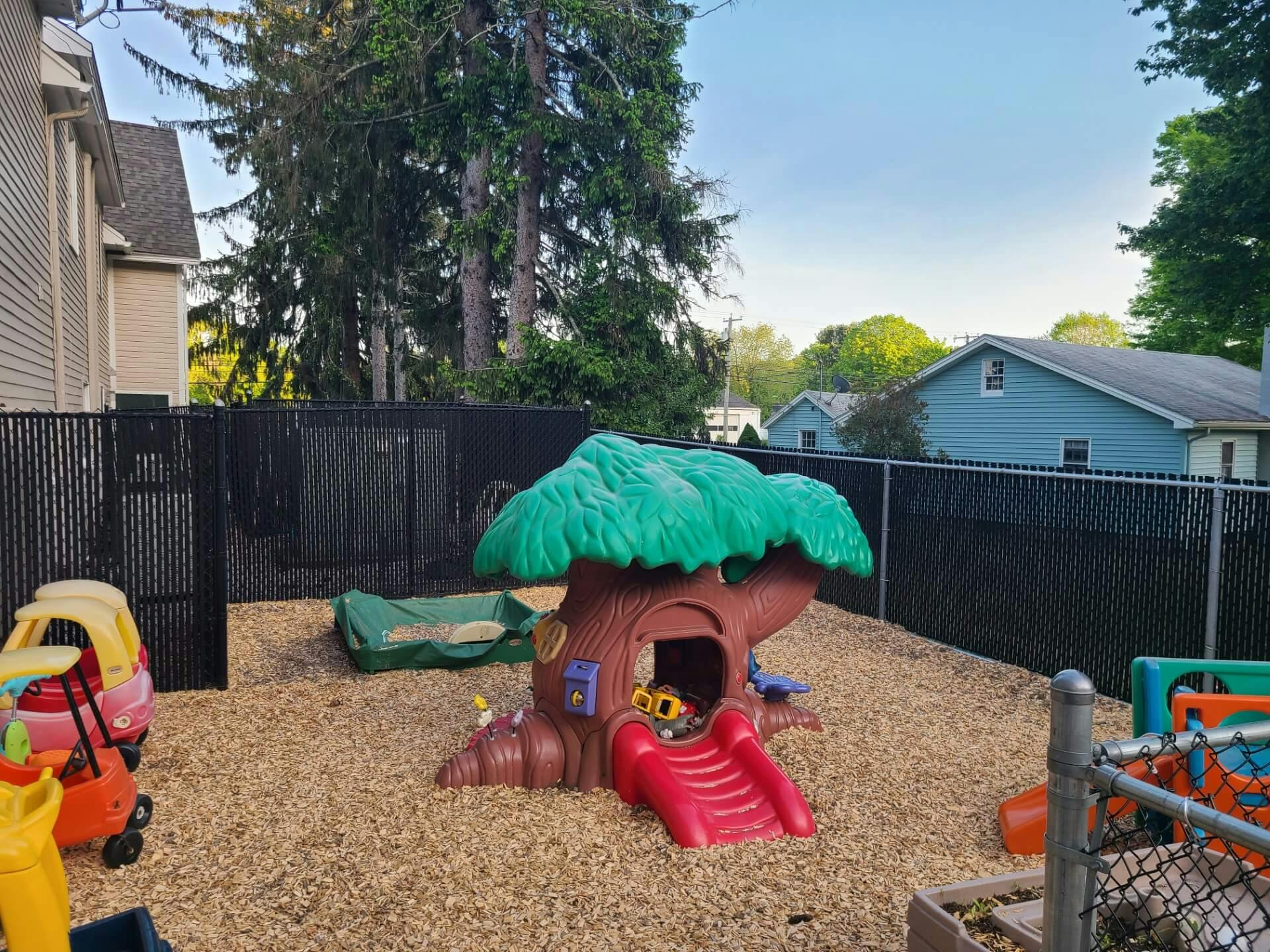Plastic play structure shaped like a tree with a red slide in a fenced playground