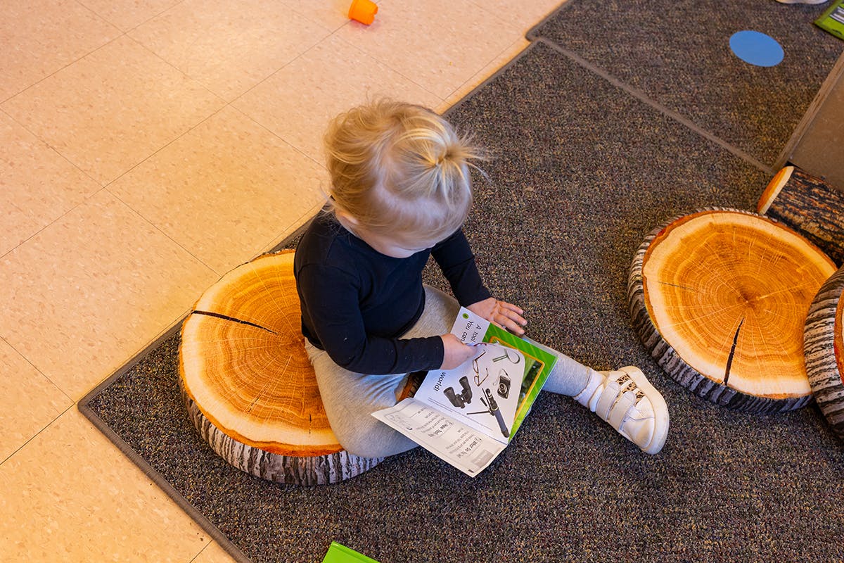 Child sitting on a tree stump cushion and looking at a book