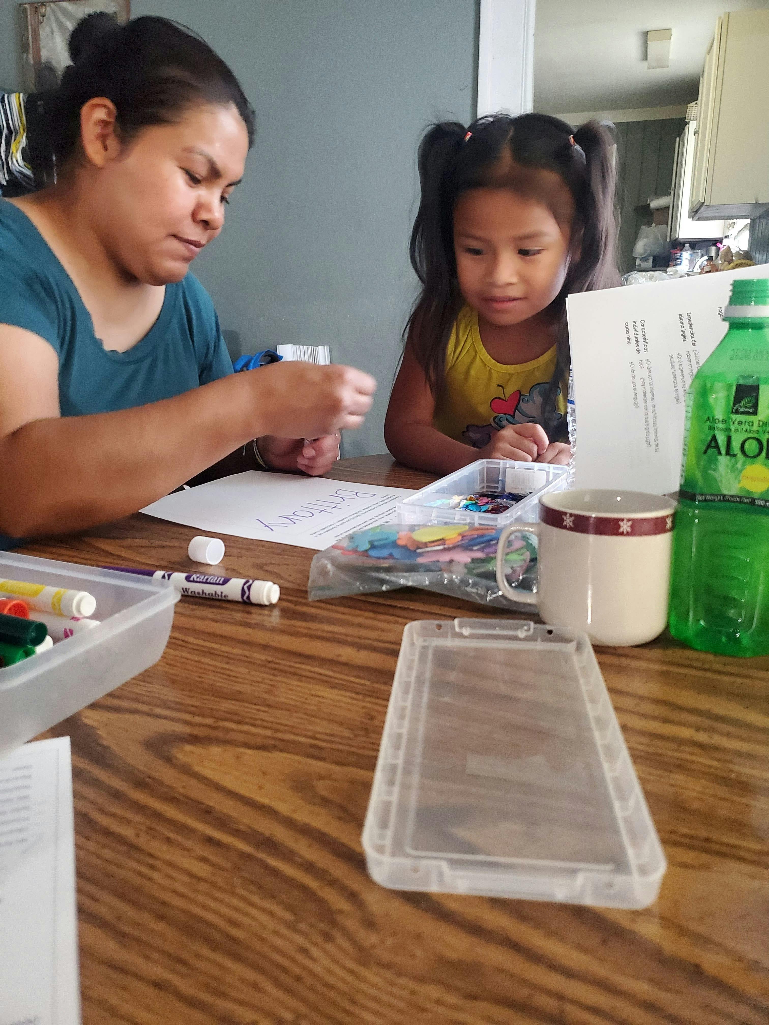 Person and child sitting at a table with art supplies