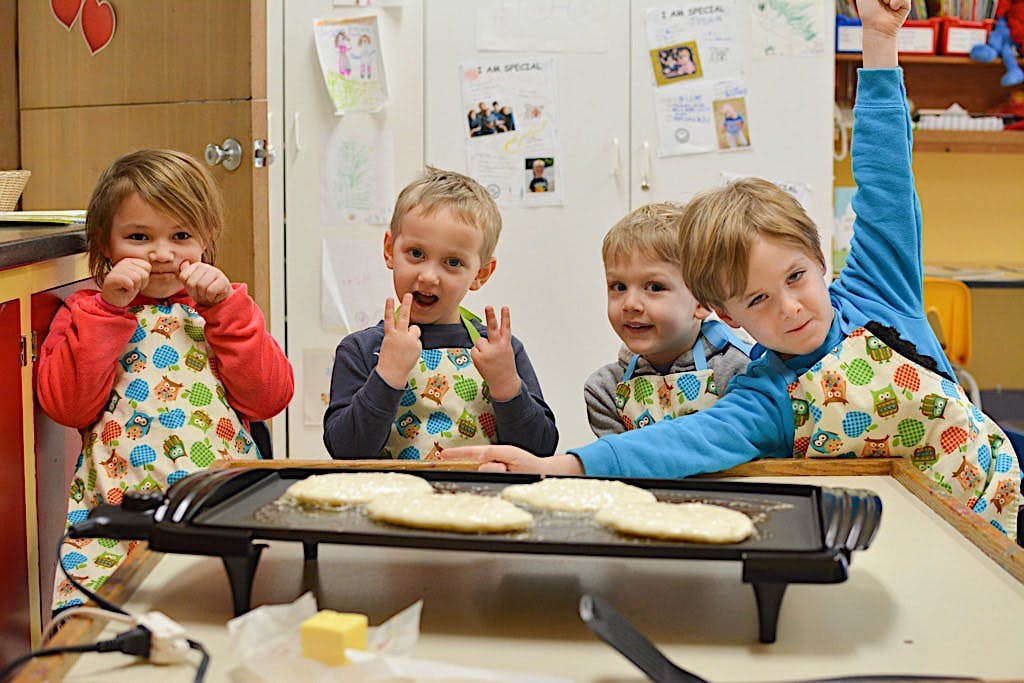 Children in aprons making pancakes on a griddle