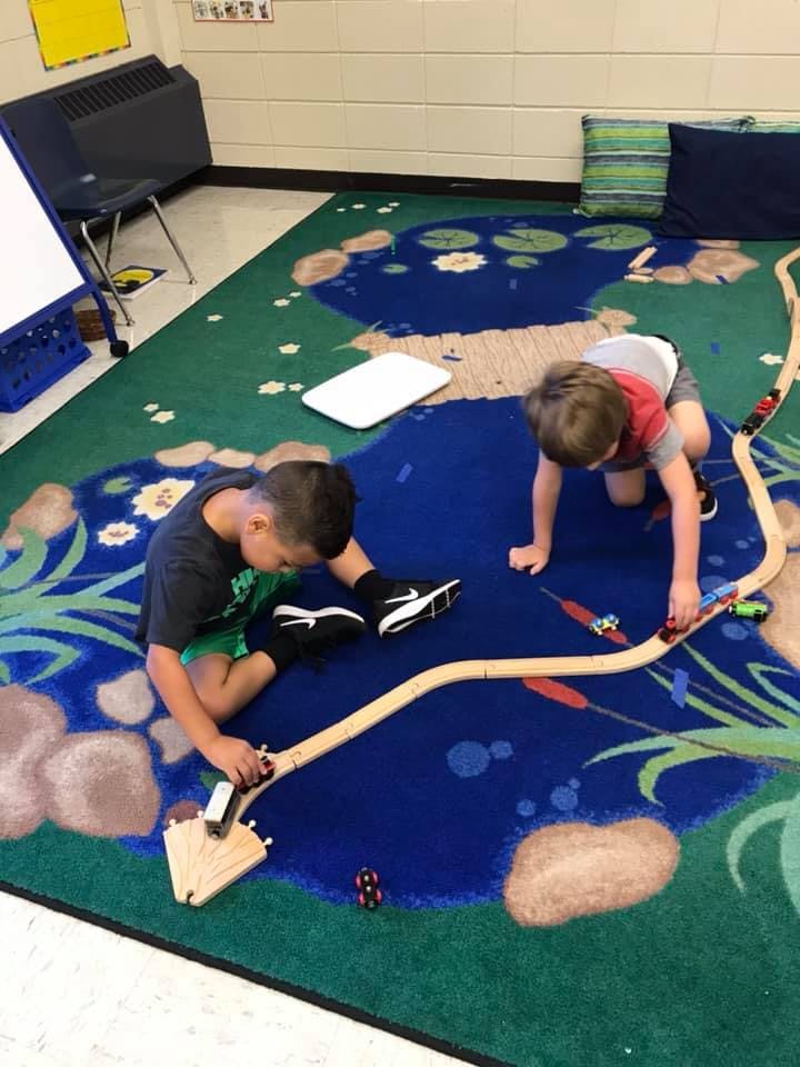 Two children playing with a wooden train set on a rug