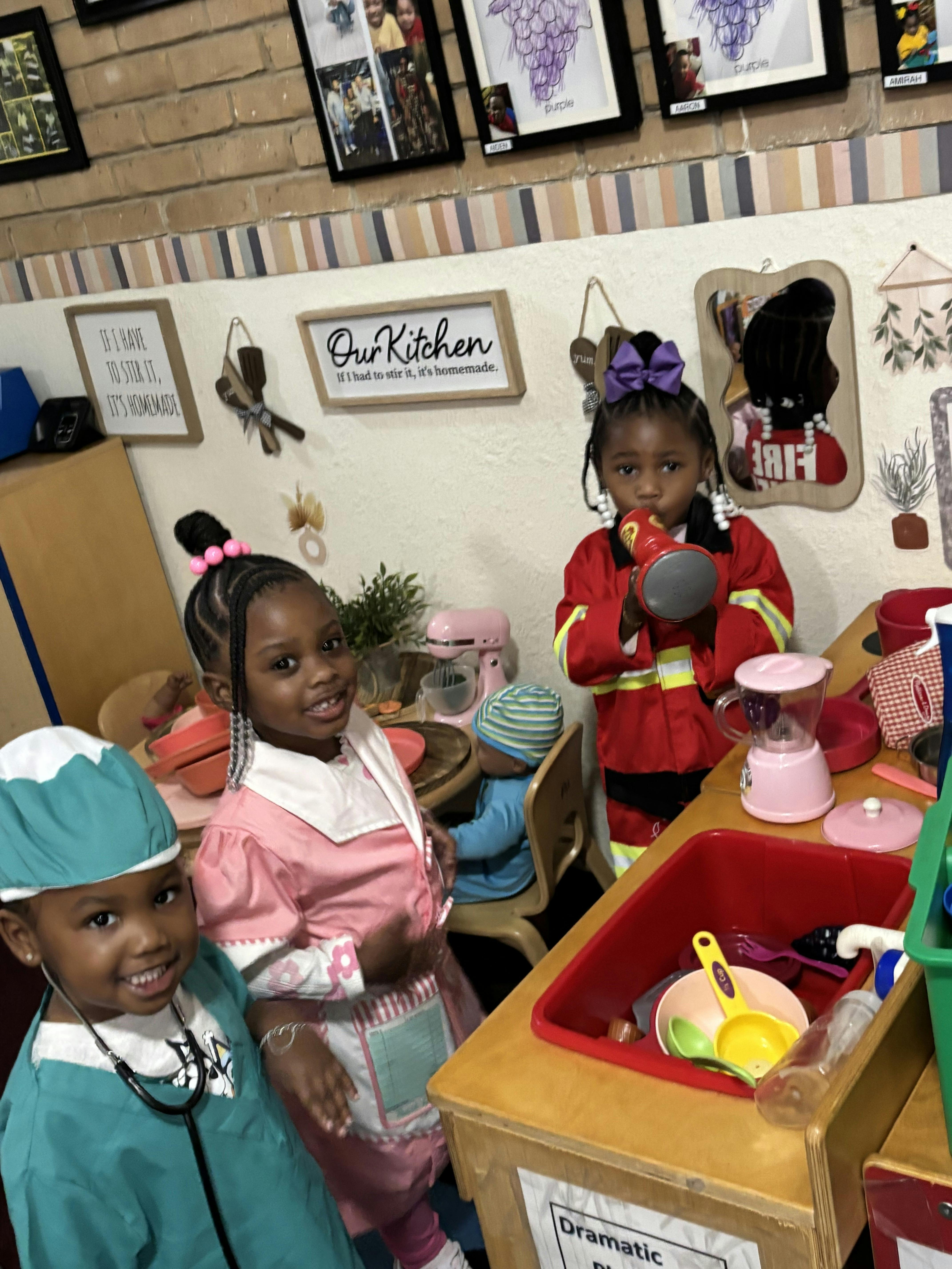 Three children in costumes playing in a toy kitchen area