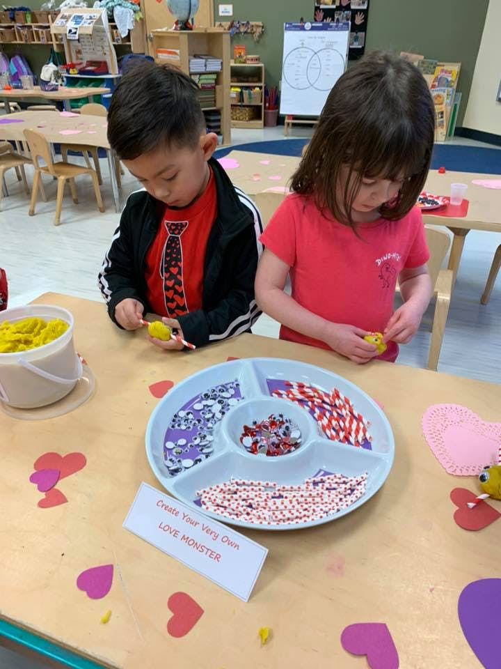 Two children decorating with sprinkles and paper hearts in a classroom