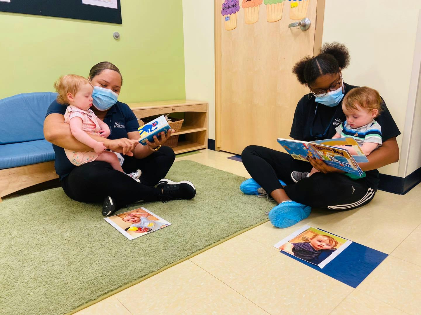 Two people wearing masks reading to two children in a classroom