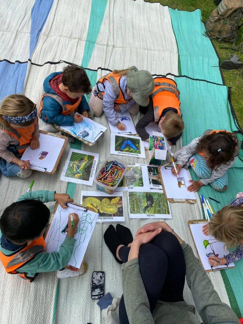 Children drawing on clipboards outdoors with reference pictures