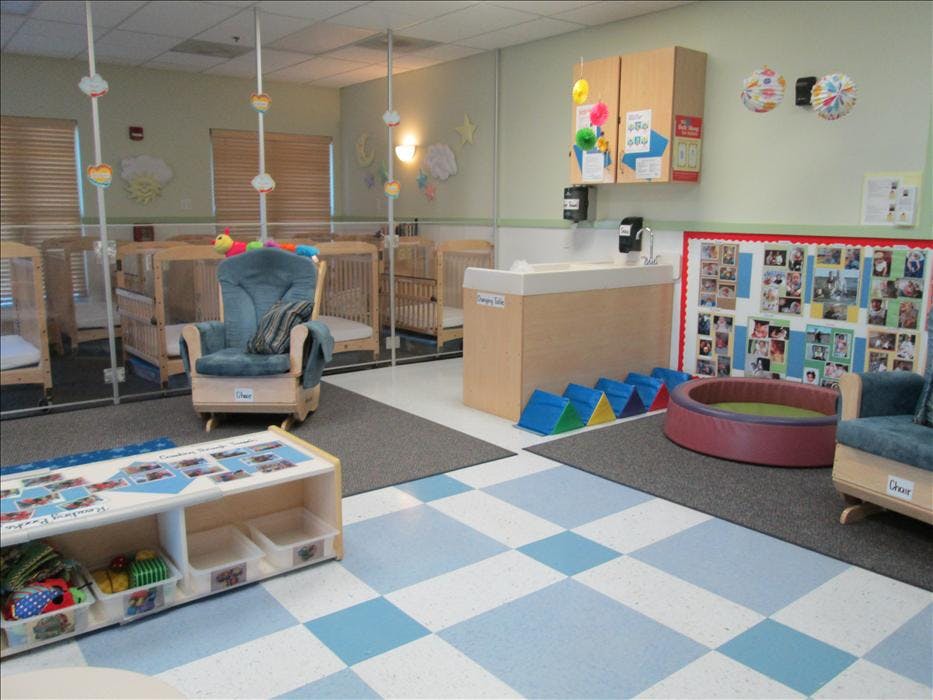 A daycare room with cribs separated by clear partitions, a changing table, and play area