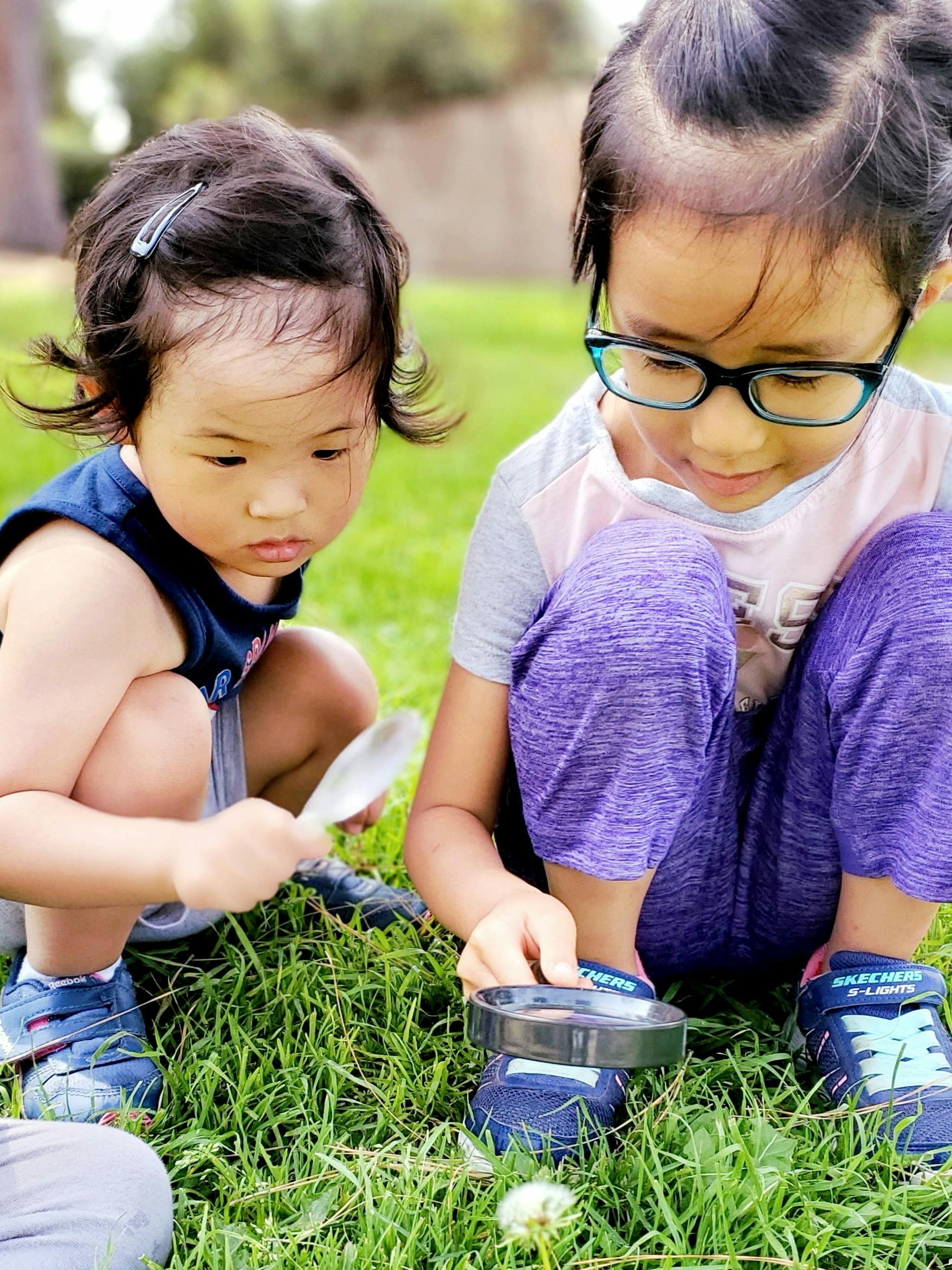 Two children on grass, one holding a spoon, the other a magnifying glass