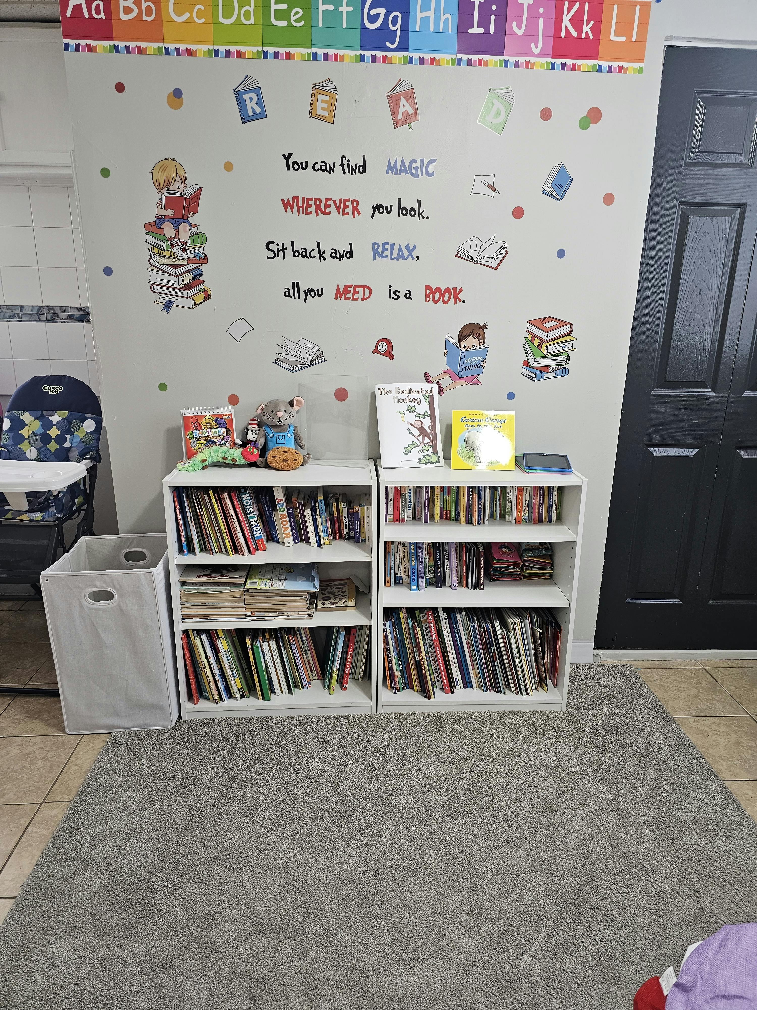 White wall with book and child decals, two white shelves filled with books, gray rug