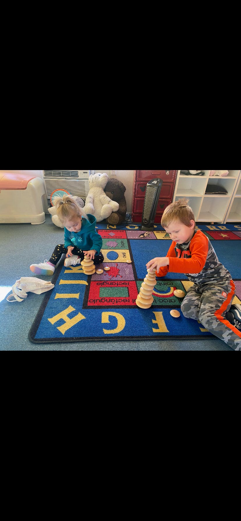 Two children playing with wooden stacking toys on a colorful rug