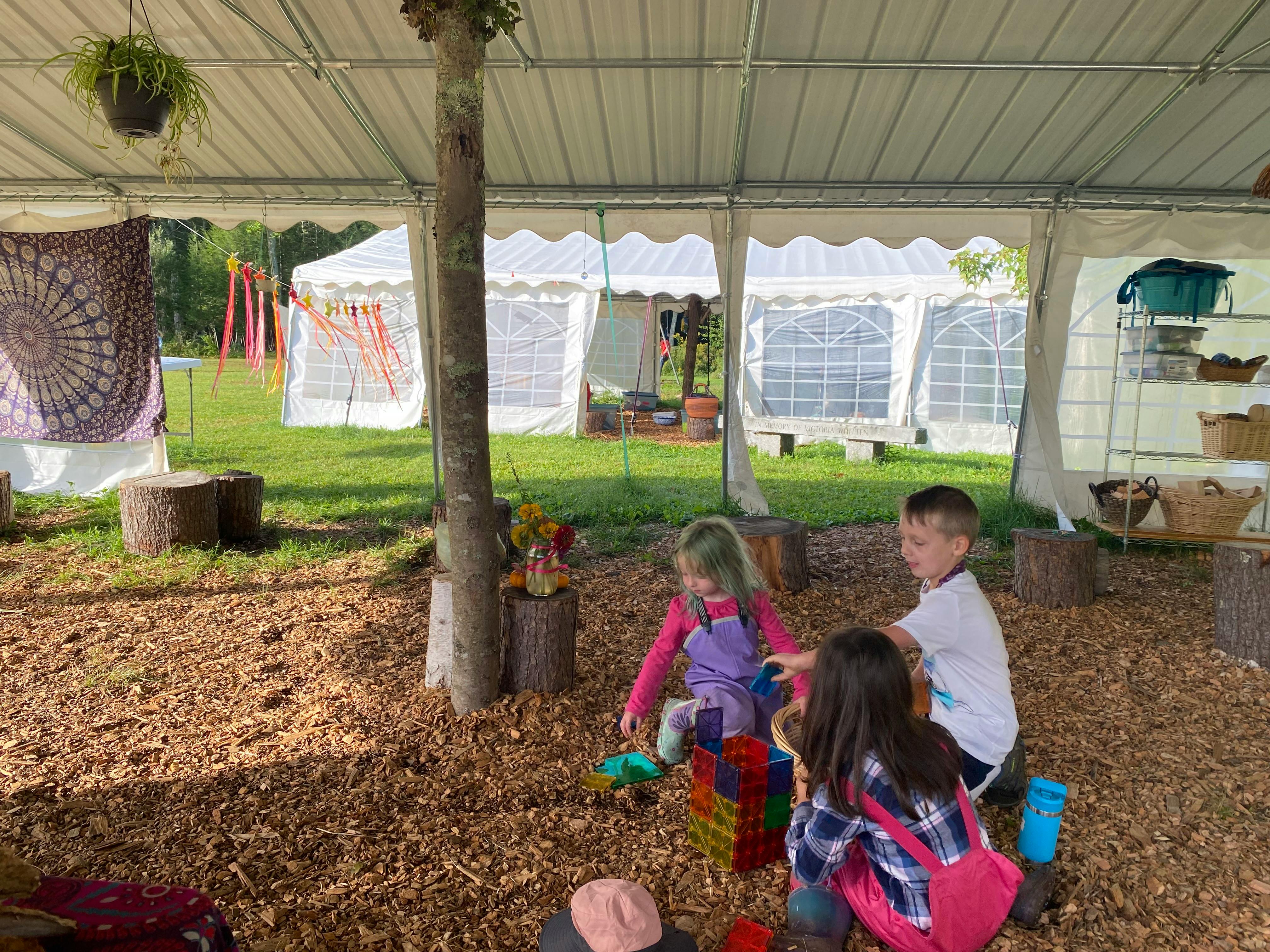 Three children playing with toys under a tent
