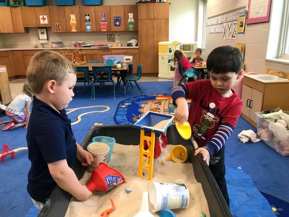 Two children playing in a sand table in a classroom