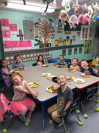 Children sitting at tables with plates of food in a classroom