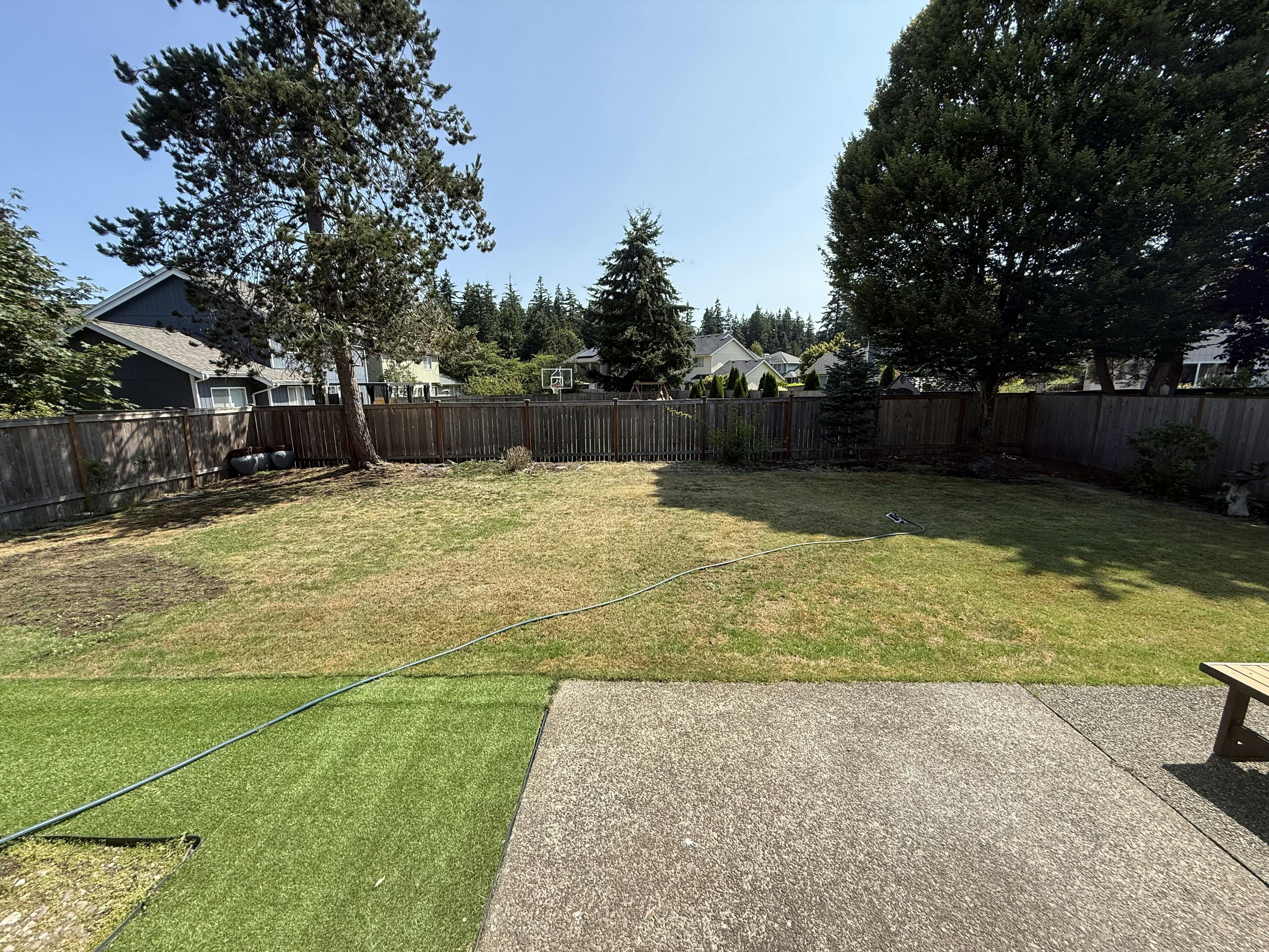 Backyard with a concrete patio and a grassy lawn enclosed by a wooden fence