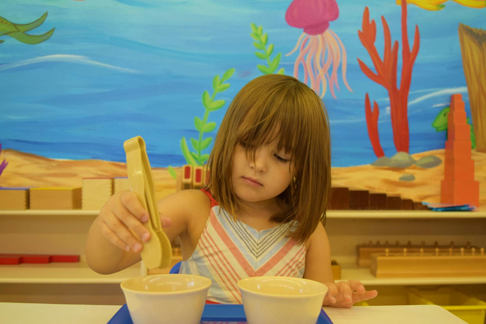 Child using tongs to move items between bowls