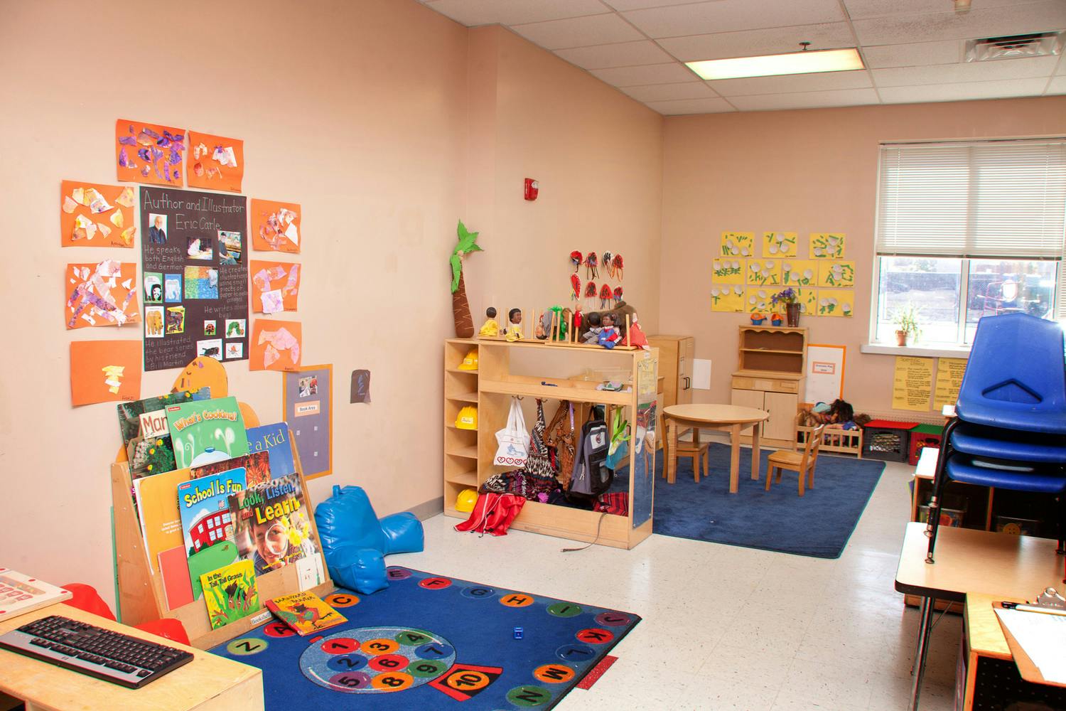 Empty classroom with small tables, chairs, and shelves with books and toys