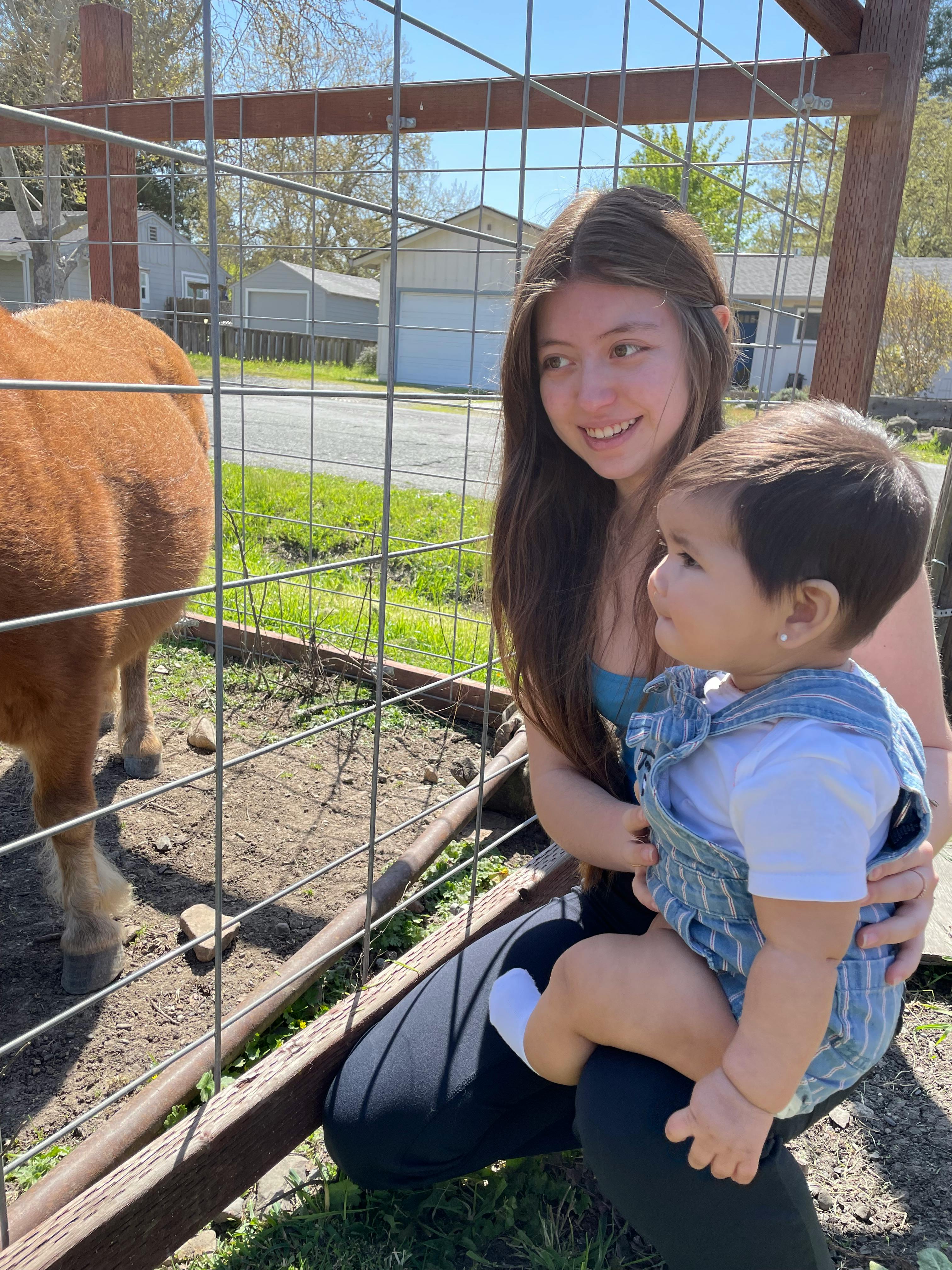 Person holding a child next to a fence with an animal