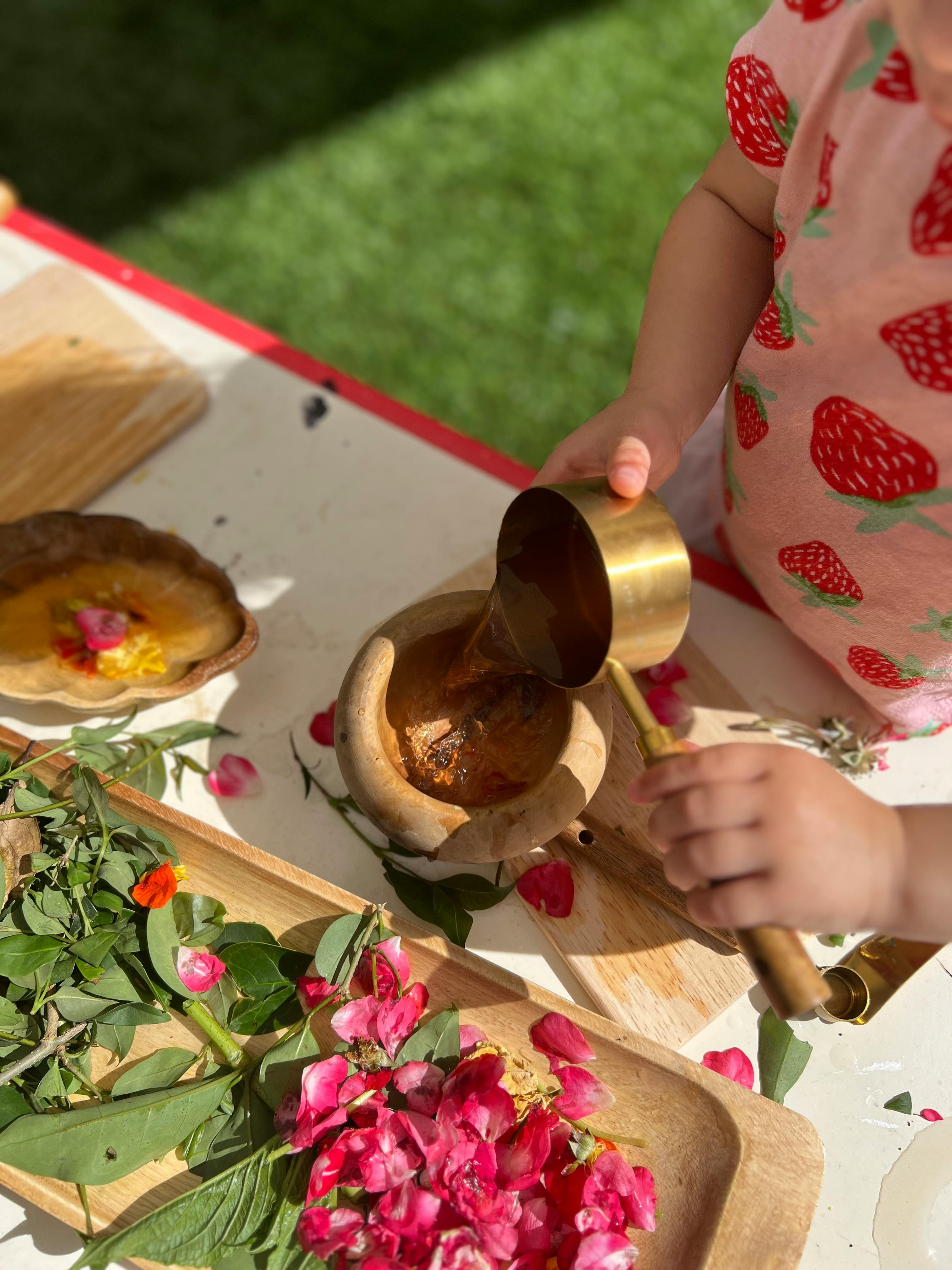 Child pouring liquid from a cup into a mortar with a pestle