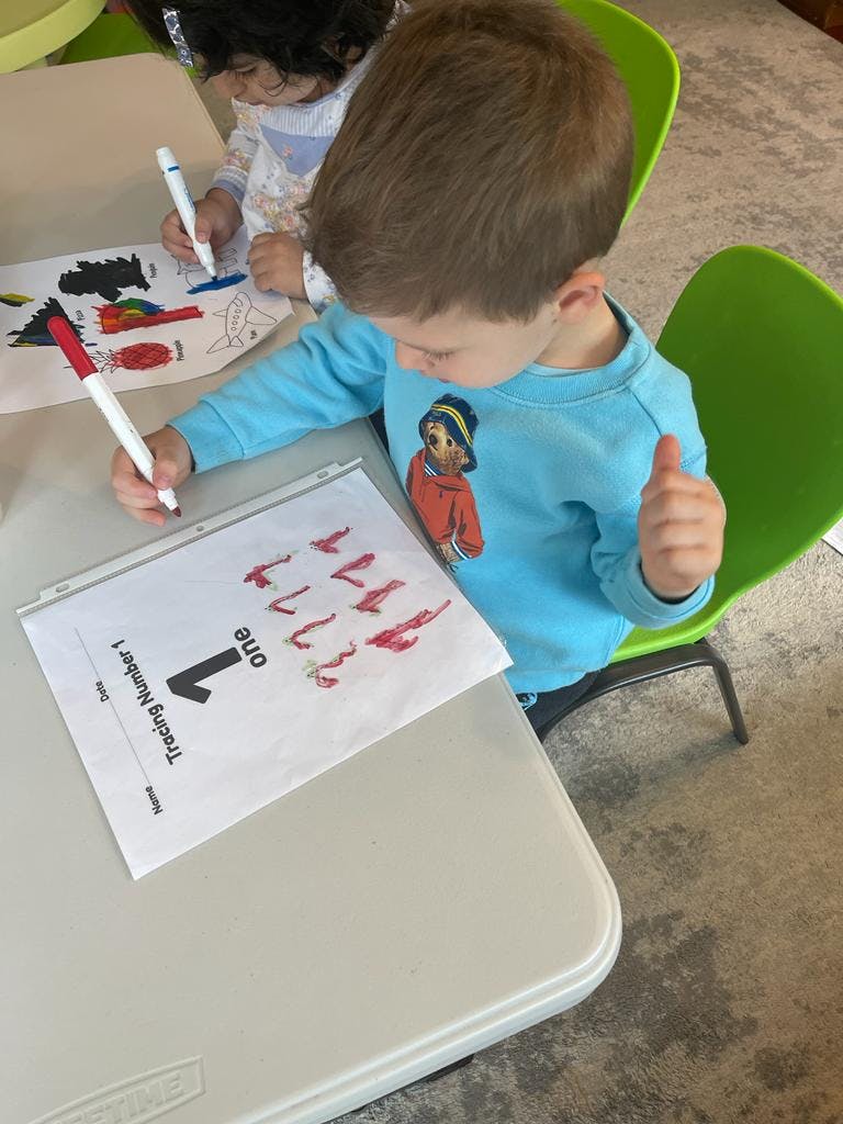 Child tracing the number one on a worksheet with a red marker